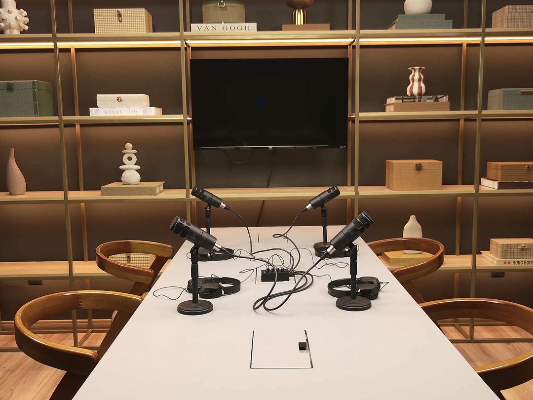 Mesa de podcast do Estúdio B · M8 vista de frente, com a estante iluminada ao fundo