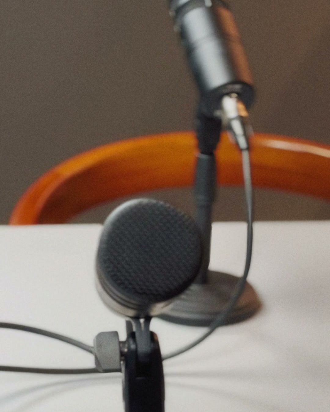 Microfone em primeiro plano sobre a mesa do Estúdio B · M8, com câmera PTZ desfocada ao fundo