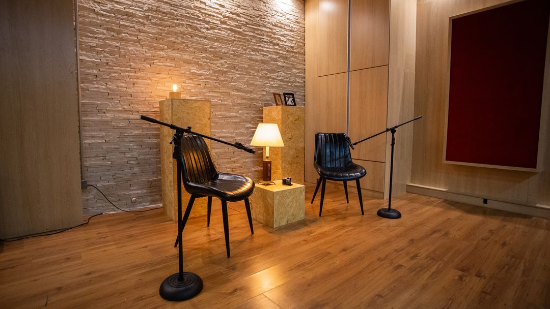 Set de podcast na sala de gravação do Estúdio A, com poltronas de couro, microfones em pedestal e luminária