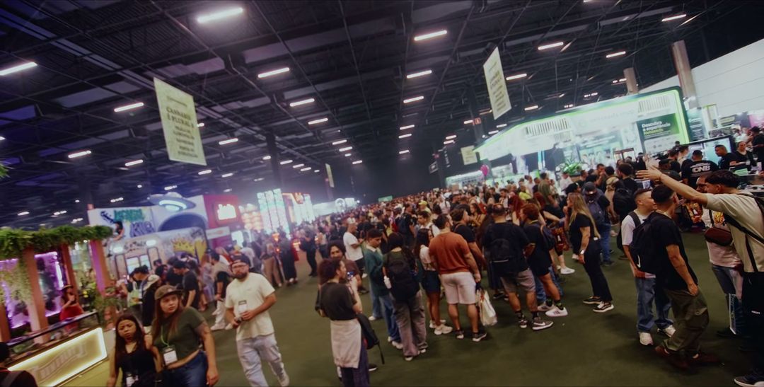 Corredor lotado de visitantes entre estandes iluminados da ExpoCannabis Brasil