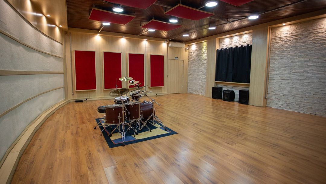 Sala de gravação do Estúdio A vista de lado, com bateria montada, painéis acústicos vermelhos e piso de madeira