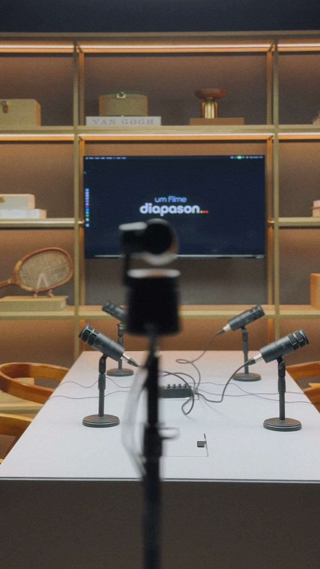 Mesa do set de podcast do Estúdio B · M8 vista de frente, com câmera PTZ, microfones e TV ao fundo