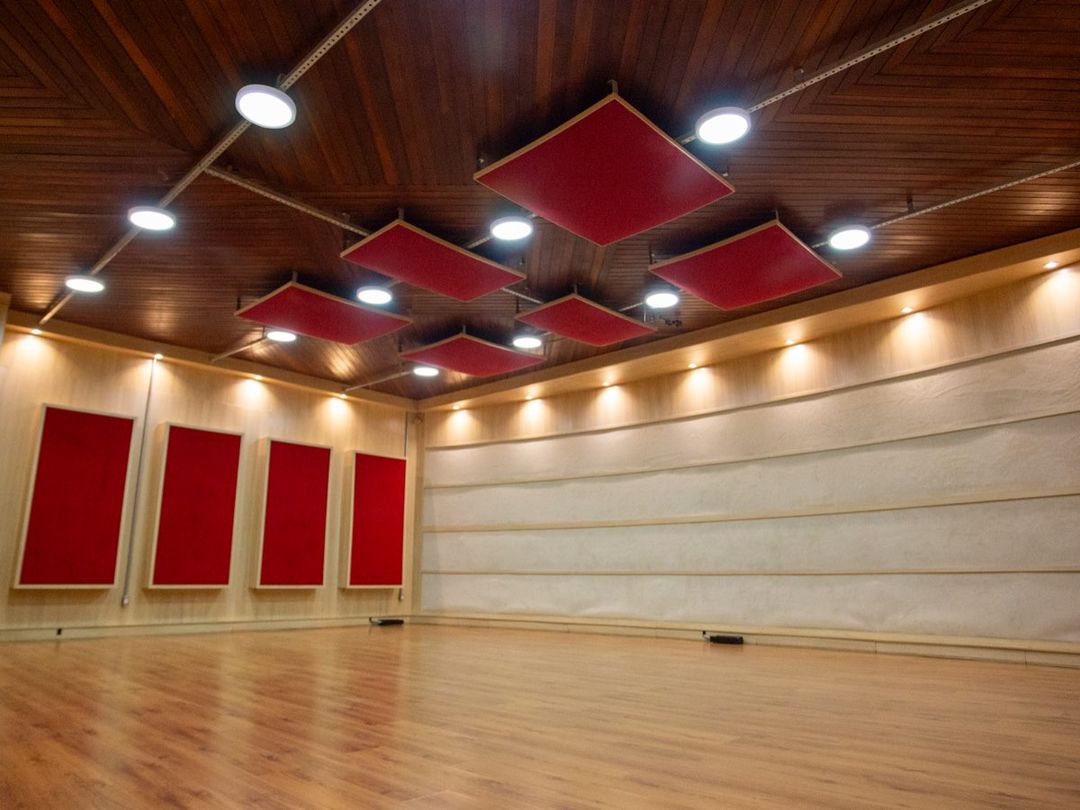 Canto da sala de gravação do Estúdio A, com painéis acústicos vermelhos e piso de madeira