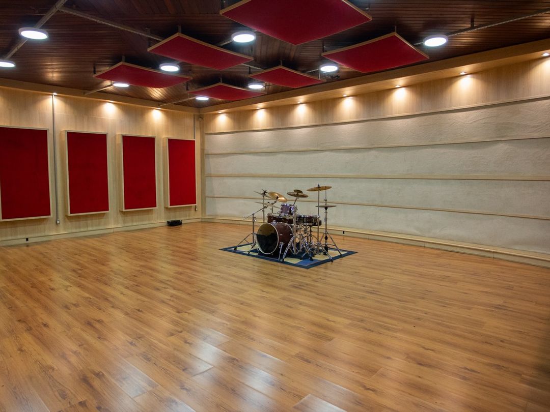 Sala de gravação do Estúdio A vista de frente, com bateria montada e painéis acústicos vermelhos